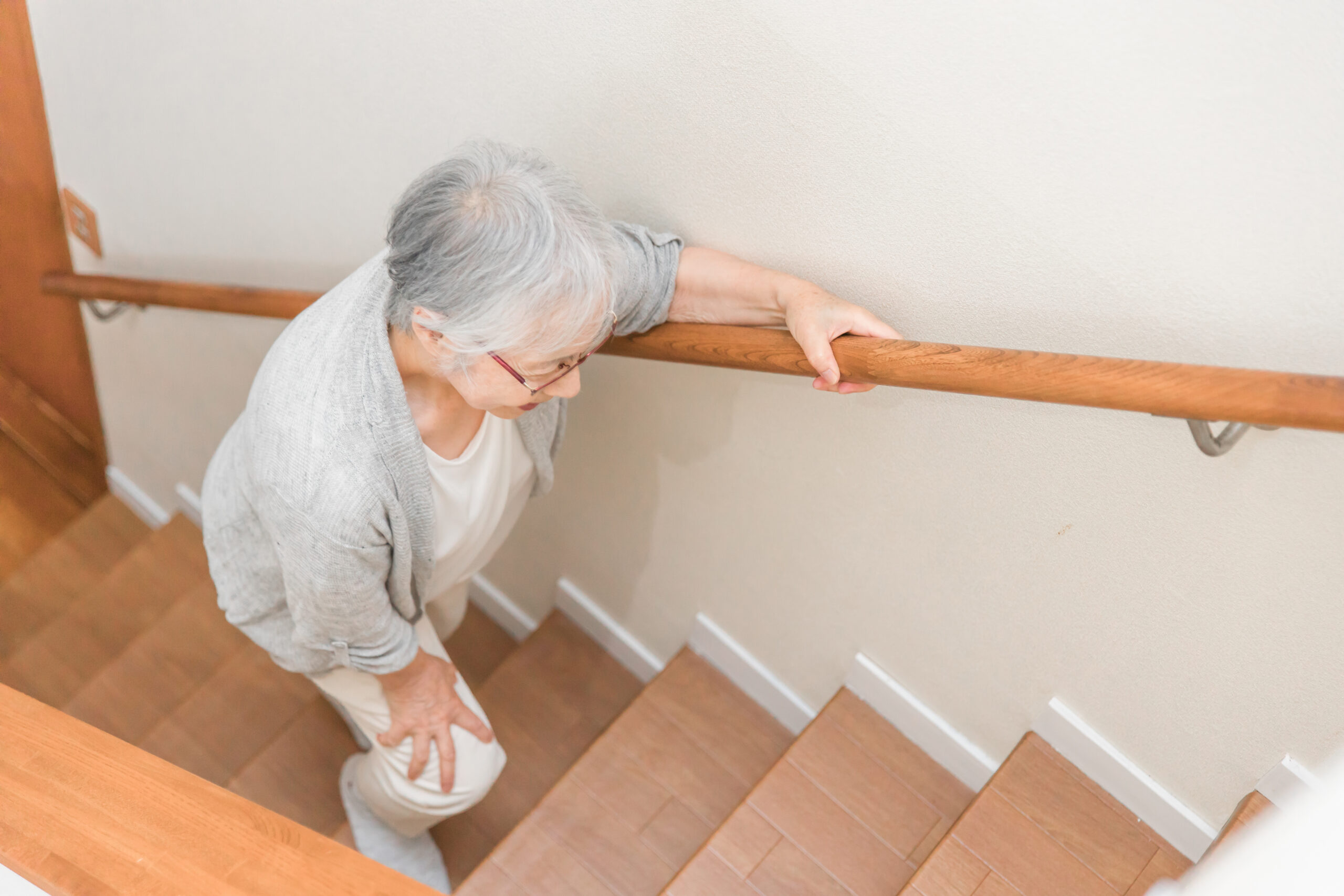 膝の痛みを感じながら階段を上る高齢女性